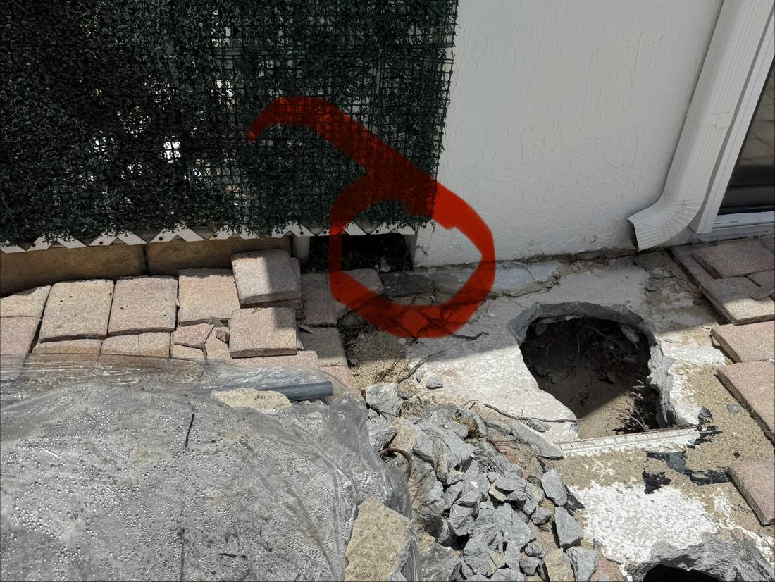 Excavation at a Weston home with the located leak marked, alongside the rock and fill that has to be cleared to reach it